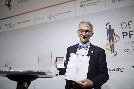 Ein Mann hält eine Auszeichnung in die Kamera.