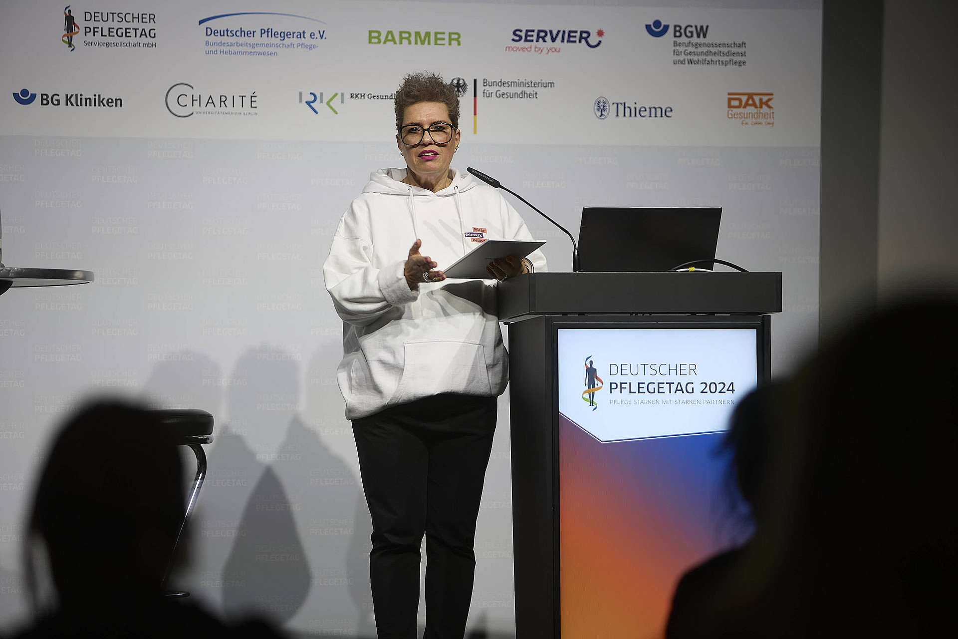 Eine Frau an einem Rednerpult vor Publikum bei einer Veranstaltung.