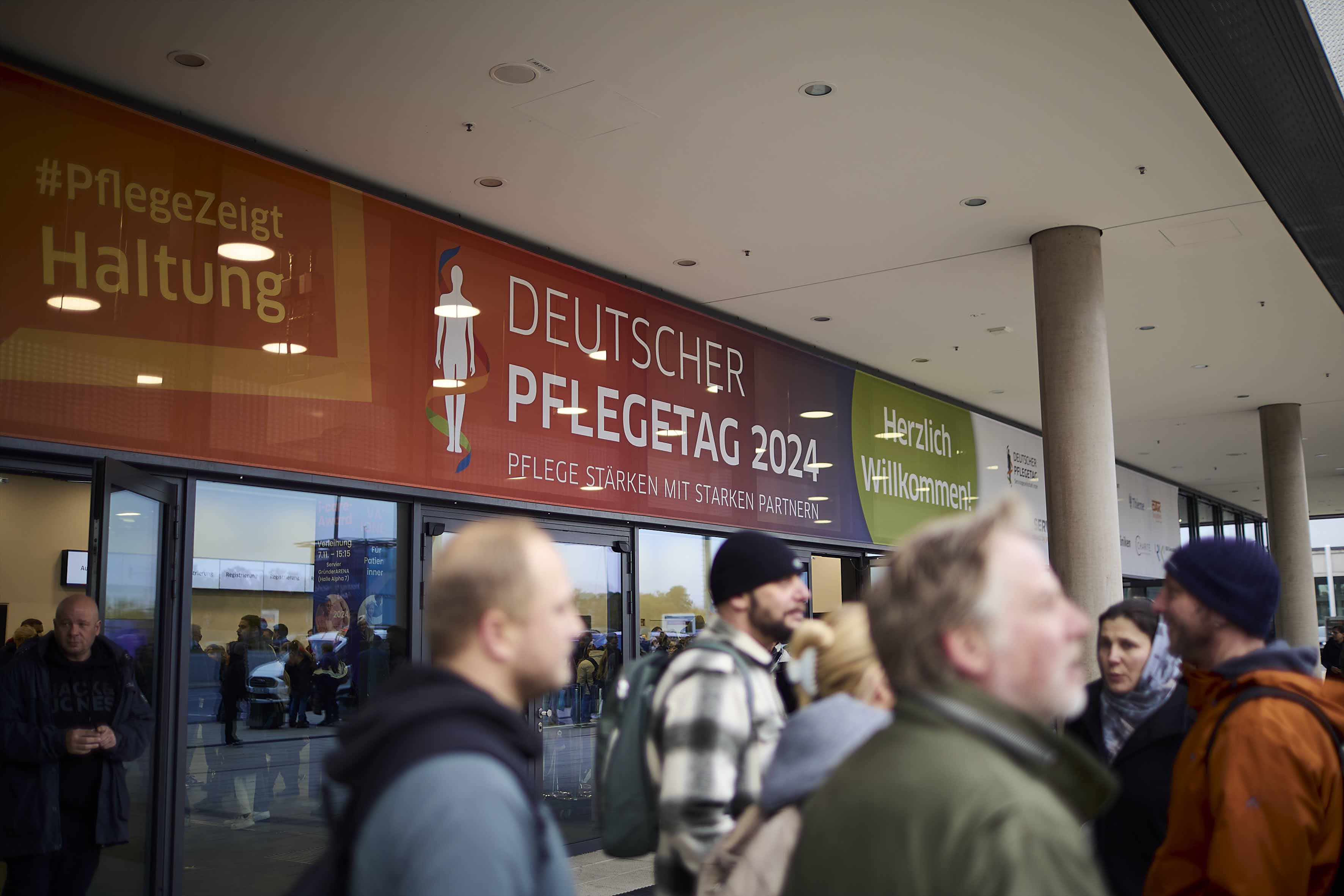 Menschen am Eingang einer Messehalle. Auf einem Banner steht Deutscher Pflegetag 2024